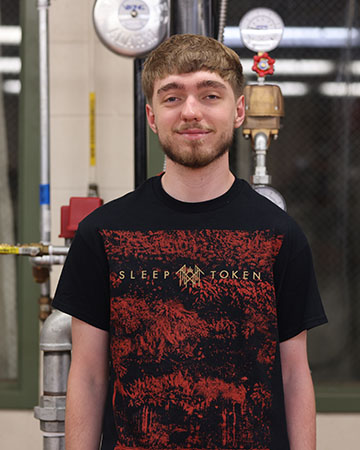 A student stands infront of a fire sprinkler system.