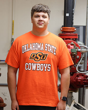 A student stands in a fire sprinkler lab dressed in an OSU shirt.