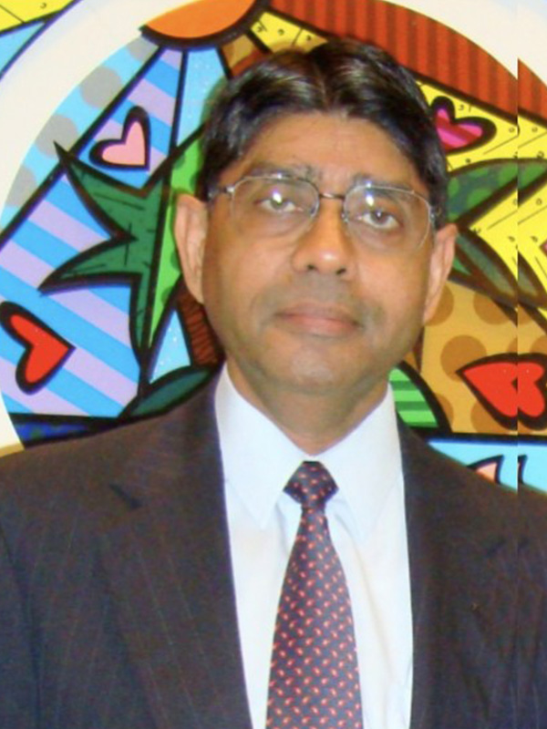 A man dressed in a black suit stands infront of a stained glass window.