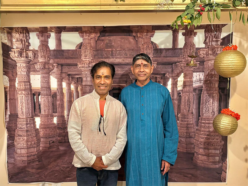 Two men dressed in traditional India garb stand infront of festive decorations.