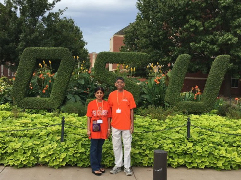 A man and woman stand infront of a topiary designed to say OSU.