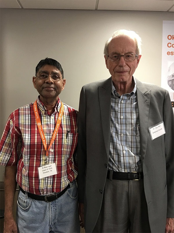Two men stand together dressed in professional attire.