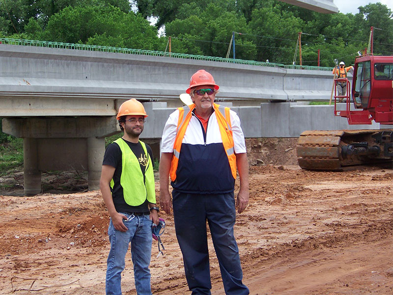 Two men in hard hats stand at a consturction site.