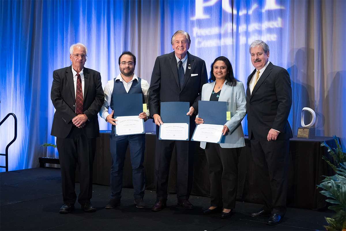 A group of individuals in formal wear stand on a stage holding certificates.