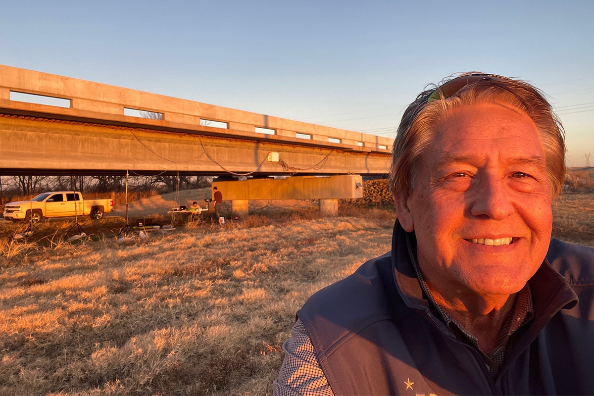 A man takes a selfie in front of a bridge that is in the middle of construction.