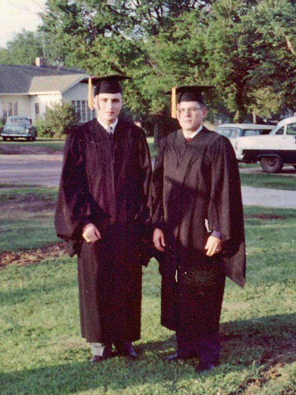 Two men pose together in full graduation garb.