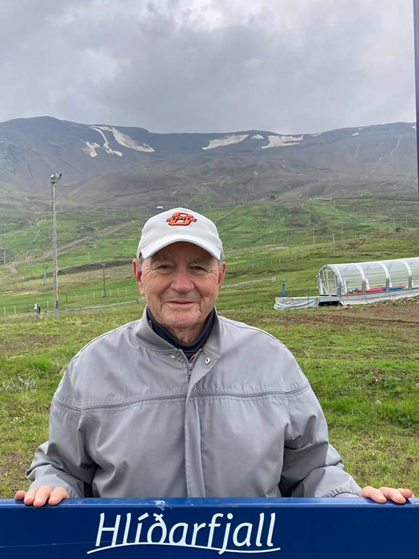 A man in a sweatshirt and hat poses infront of a landmark sign in Iceland.