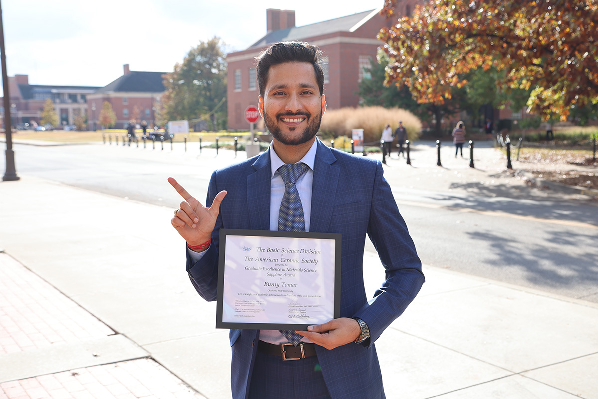 Bunty Tomar stands outdoors holding an award and giving the Go Pokes hand signal at Oklahoma State University.