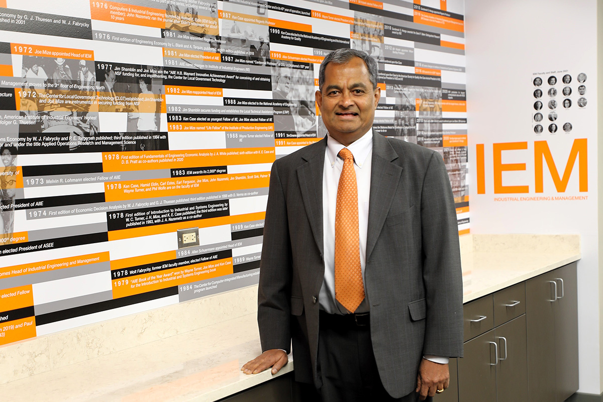 Dr. Sunderesh Heragu stands in the IEM conference room in front of an orange, black and white wall