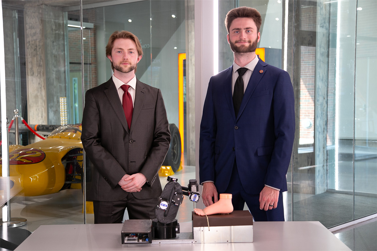 Trevor Fogleman and Joel Quarnstrom standing behind a table with a foot on it.