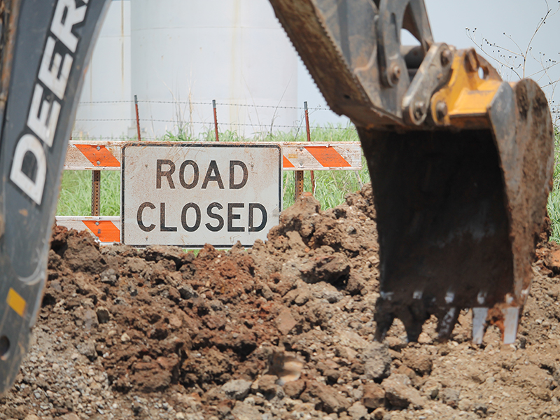 Excavator arm with road closed sign in the background