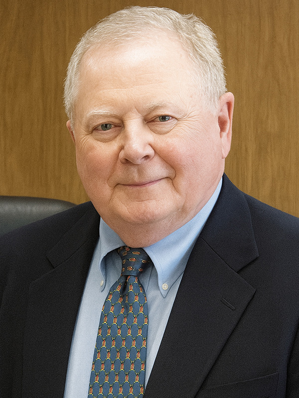 A professional headshot of a man in a navy blue suit.