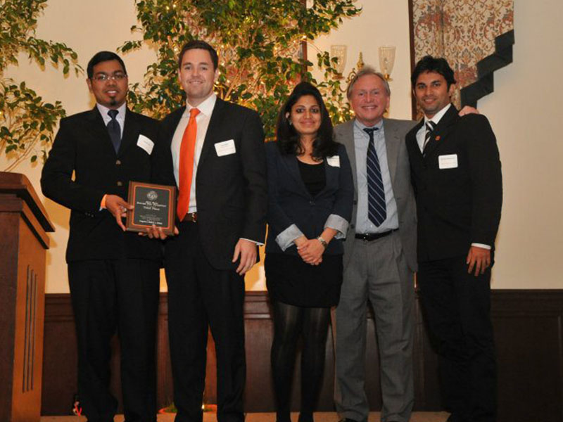 A group of people dressed formally stand on stage while one holds an award.