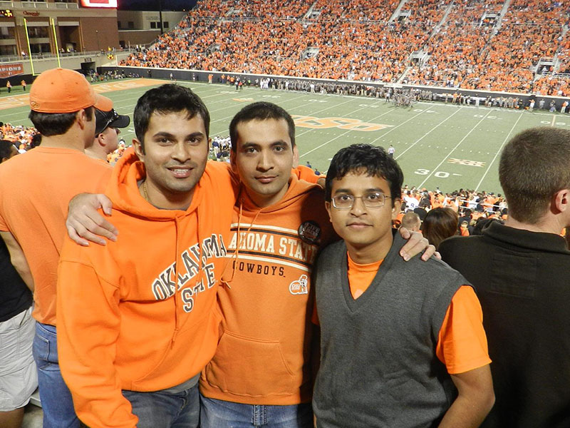 Three people stand together in the stands of Boone Pickens wearing Oklahoma State University orange.