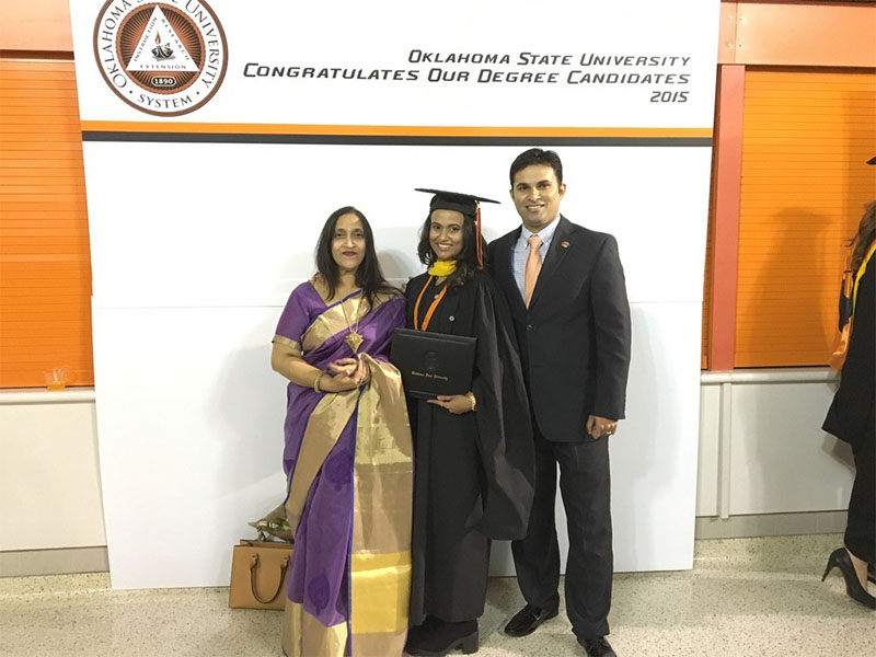 A man and woman dressed formally stand with a graduate in their cap and gown, holding their degree.
