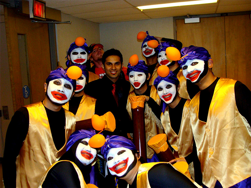 A group of individual in colorful makeup and costumes posing with smiles in a backstage area.