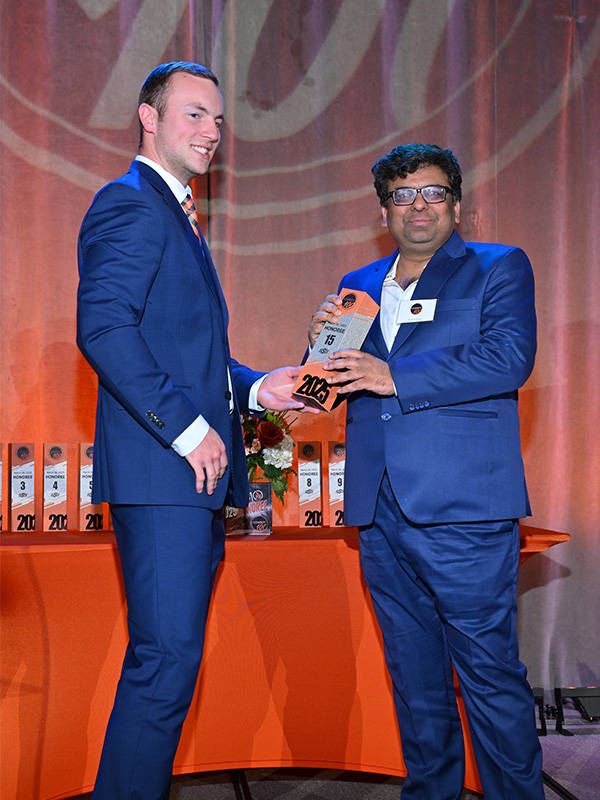 One man handing another man an award on stage, both are dressed in suits and the background is OSU orange.
