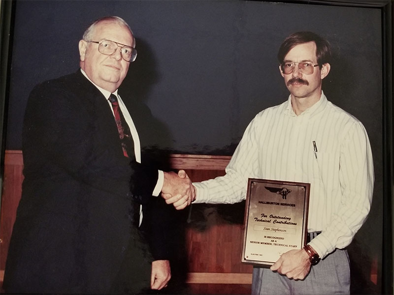 Stan shaking the hand of a man in a black suit, receiving an award. 