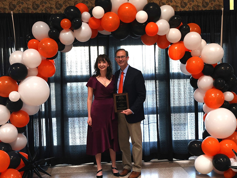 A man and a woman stand smiling after the man received an award. 