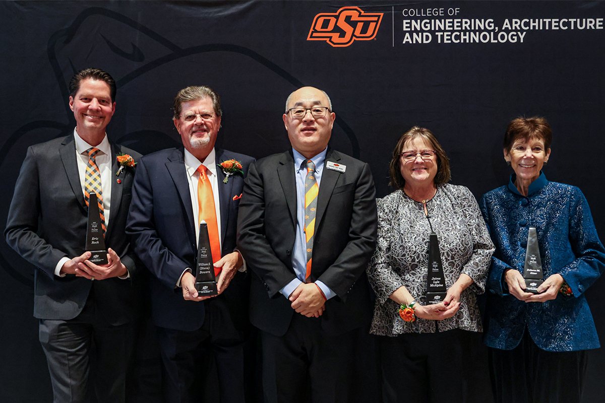five individuals in formal attire standing in front of a black backdrop.