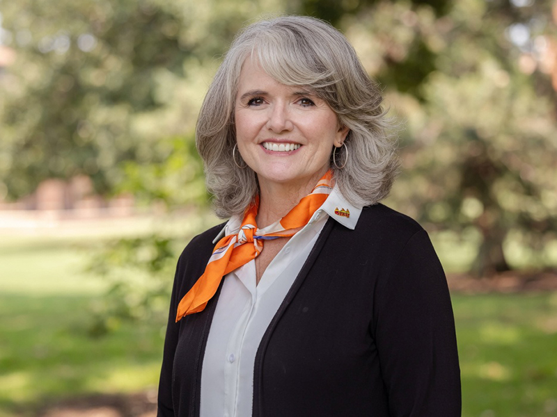 Headshot image of Dr. Leslie Stockel In an outdoor setting wear black and white clothing.