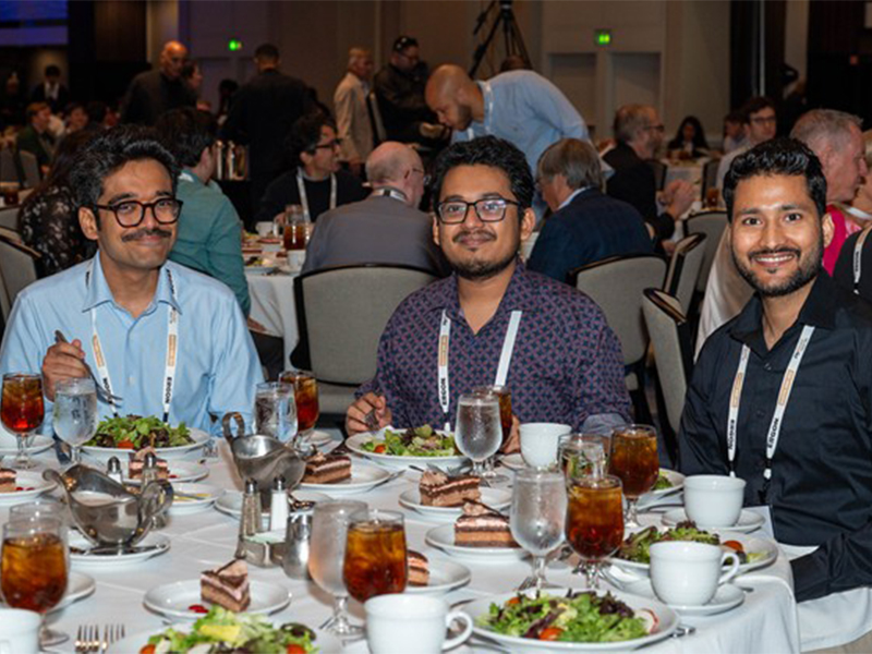news-5-25-2.jpg Three gentlemen in button up shirts sitting together and smiling at a formal dinner