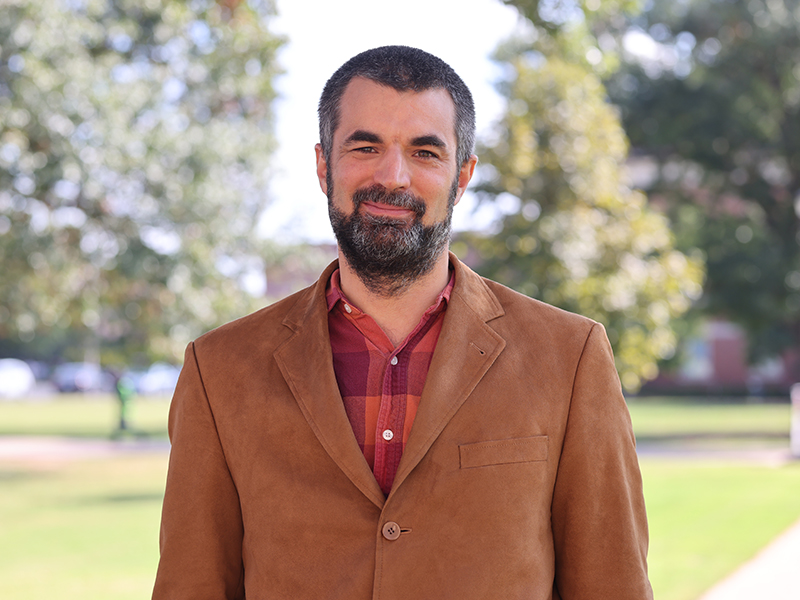 headshot image of Christian Bach wearing a brown suit jacket standing outdoors